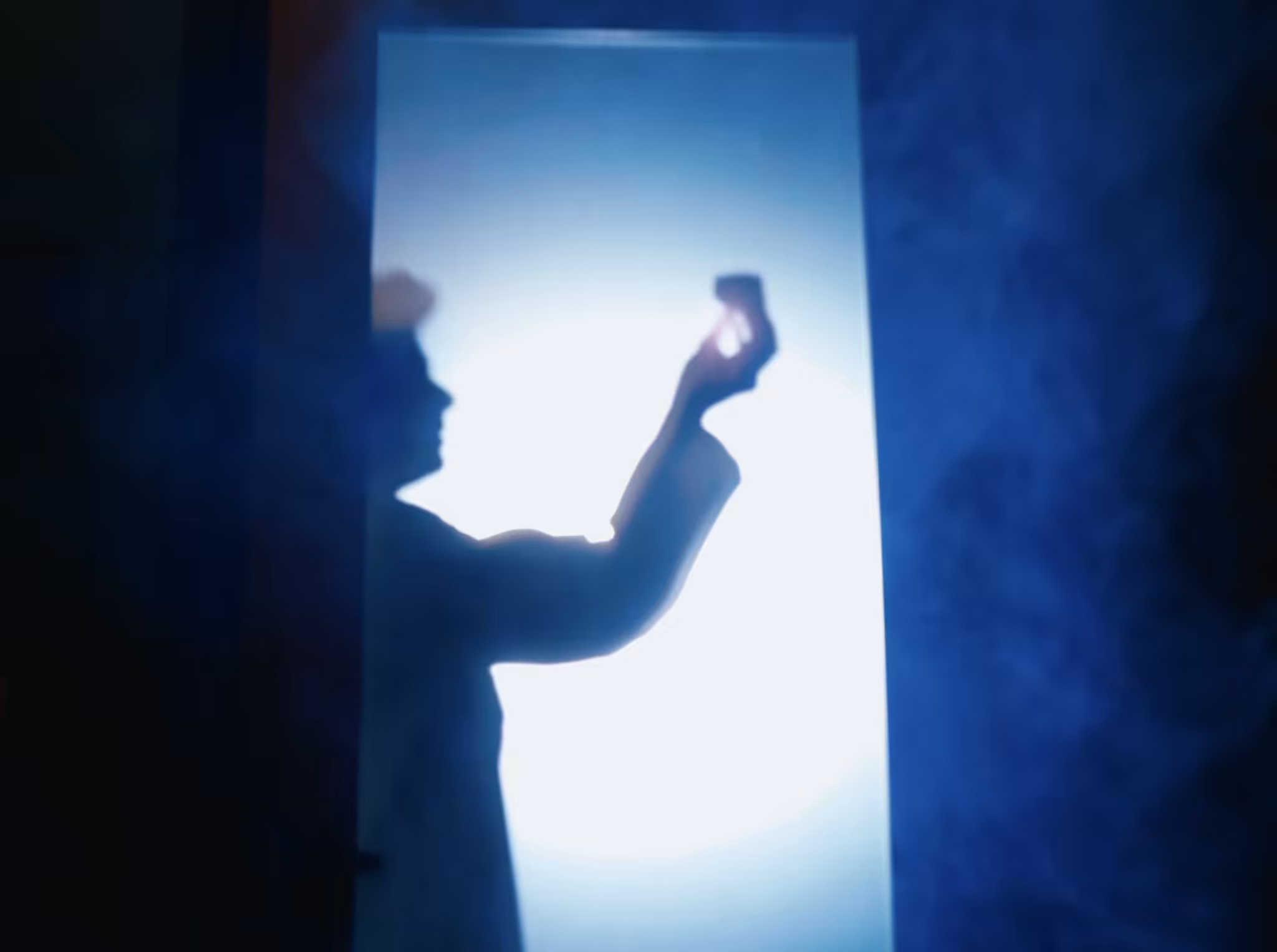 Silhouette of a person reaching up against a glowing white panel in blue haze